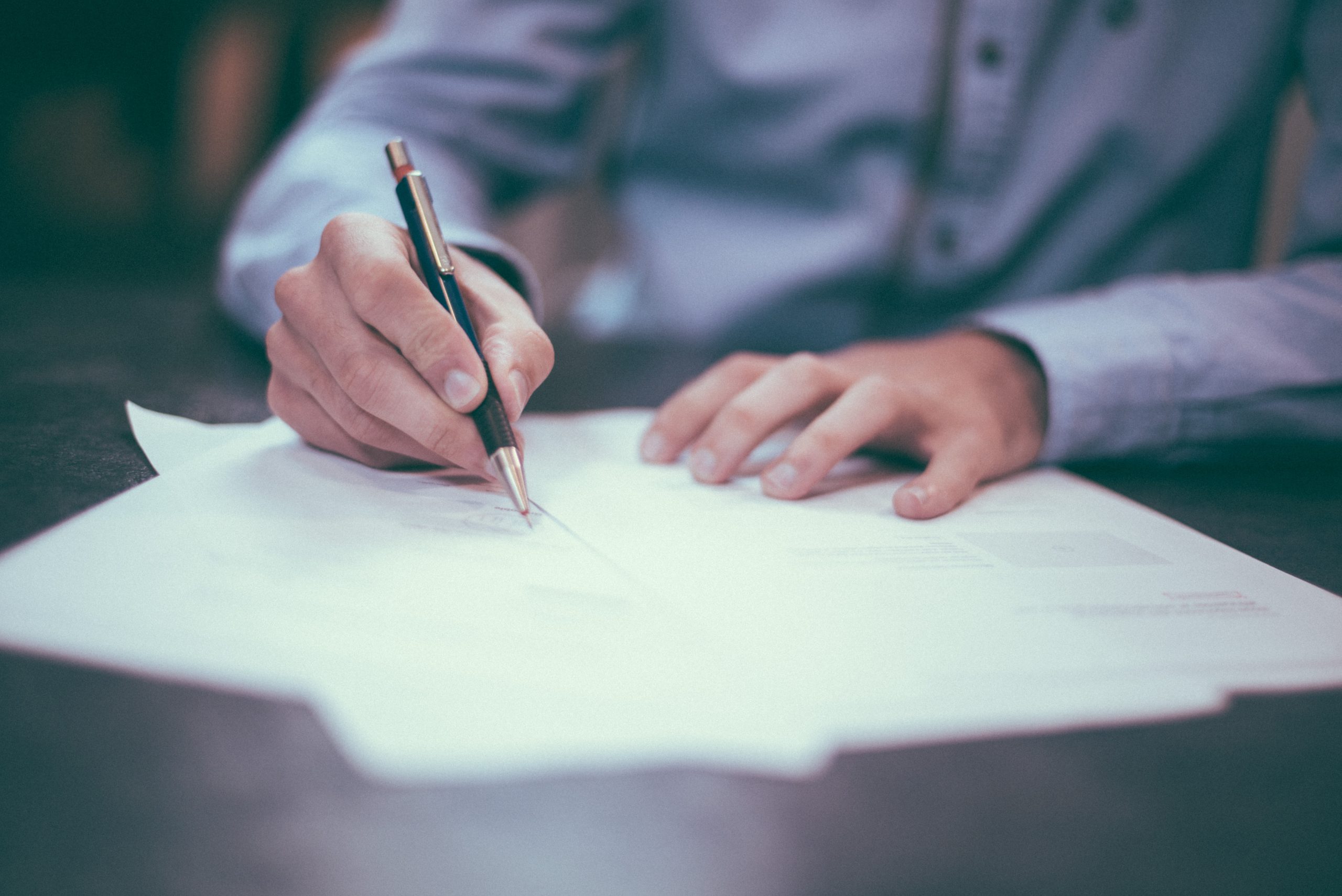 a man in a blue shirt writing with a nice pen on multiple sheets of paper