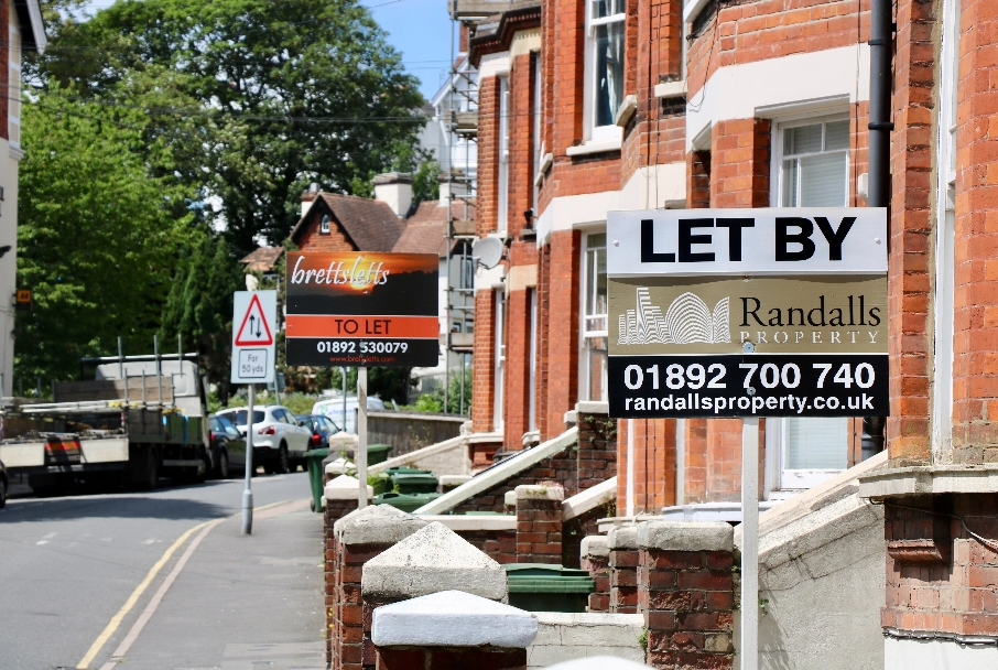 residential street with orange brick houses and a 'let by' sign outside the house in the foreground