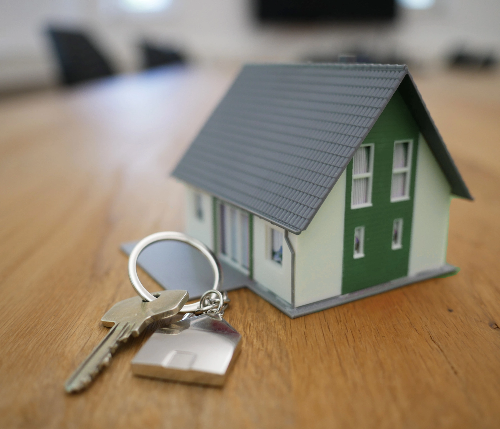 set of house keys on a wooden desk with a small green plastic house as a keyring.