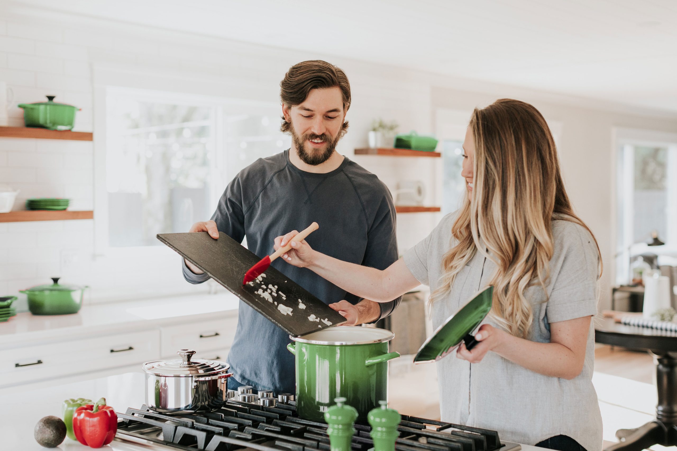 smiling young couple cooking in a white kitchen with dark green crockery